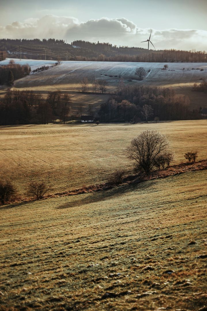 Feld im Sonnenschein mit tauendem Schnee und Windrad am Horizont